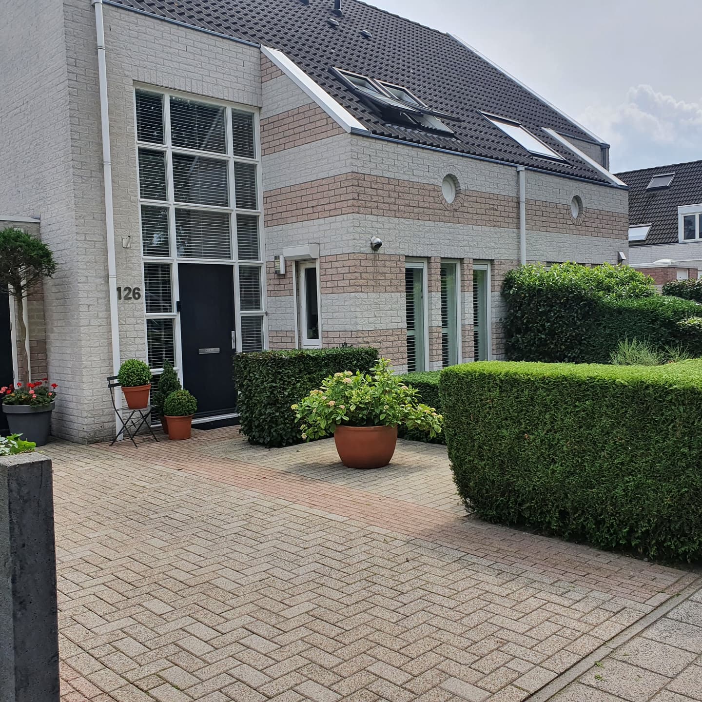 Voortuin met klinkerbestrating, geknipte hagen en potten voor een bakstenen woning
